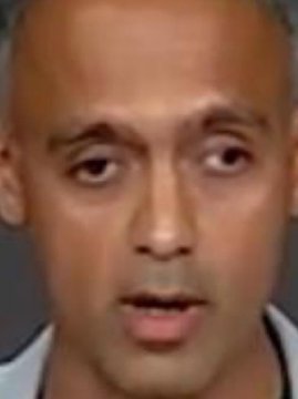 A low-resolution portrait photo of a bald man with dark eyes looking directly at the camera.