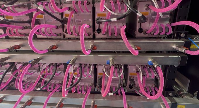 A close-up photograph of industrial equipment featuring numerous bright pink corrugated hoses connected to metal components and tubing arranged on racks.