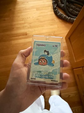 A hand holding a graded Topps 'Pencil Chump' Pokémon card in a protective slab above a wooden floor.