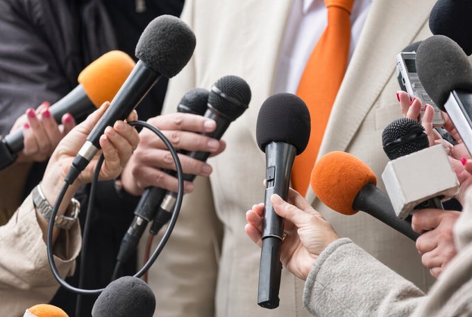 A swarm of hands thrust forward holding various microphones and recording devices toward an unseen subject, capturing a chaotic press conference moment. The image humorously illustrates the meme's punchline by depicting the overwhelming scrutiny one faces when asked about their trading activities.