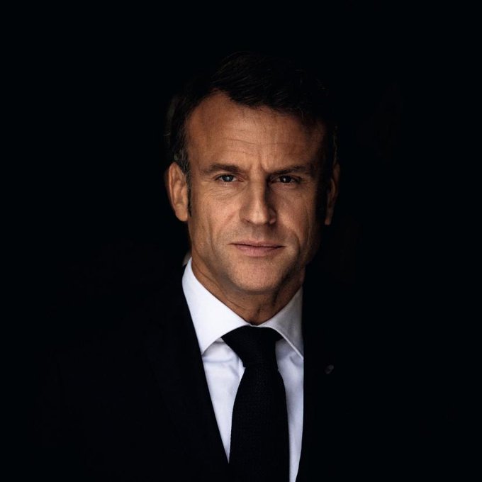 The image shows French President Emmanuel Macron in a dark suit with a black tie against a black background, his serious expression conveying gravity and introspection.

The caption "Le sang de qui?" (Whose blood?) paired with this somber portrait of Macron likely alludes to a politically charged question about responsibility or sacrifice, with Macron's pensive, almost haunting expression reinforcing the weight of the inquiry.