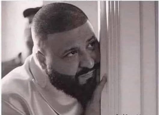 A black-and-white close-up photo shows a bearded man pressing his face against a doorframe with a wide, slightly strained smile, evoking the feeling of someone being cornered or overwhelmed. The image humorously captures the exhaustion expressed in the post about the relentless pressure crypto developers face from impatient community members asking for updates, KOLs, and promises to be fulfilled.