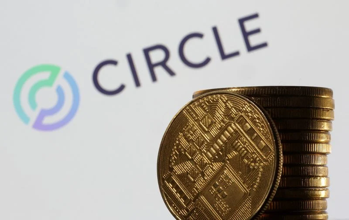 A photograph showing gold-colored coins stacked in front of a white backdrop displaying the 'CIRCLE' logo, referencing the Circle cryptocurrency/stablecoin company.