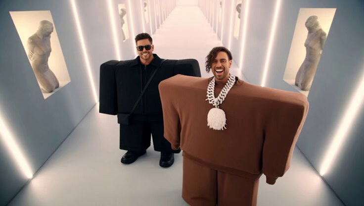 The image features two men dressed up as cartoon characters, wearing oversized clothing that resembles a bear or a robot. They are standing next to each other in an empty hallway with white walls and a gray floor. The caption of the image includes the words "good morning putting in 2x the effort to survive this market" and "@SherhanEth". This suggests that the two men dressed up as cartoon characters might be participating in some sort of event or performance, possibly related to the post's theme.