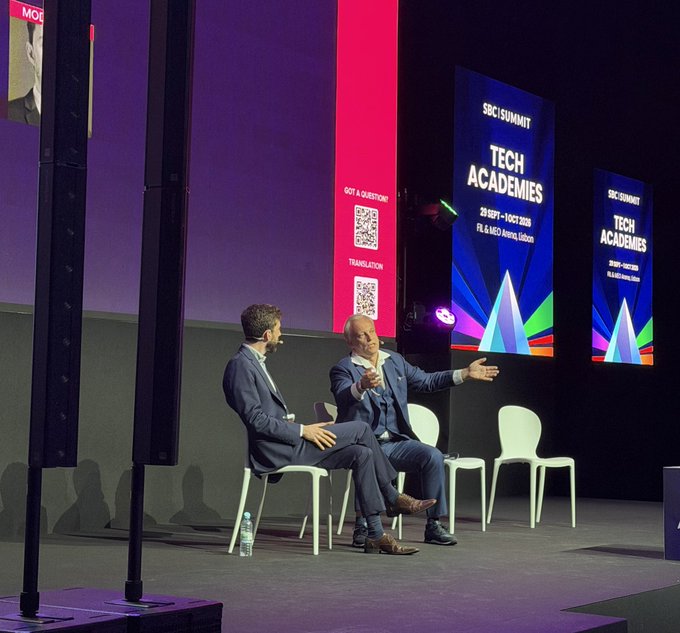 Two men seated on stage at the SBC Summit Tech Academies event (29 Sept - 1 Oct 2020) at FIL & NEQ Arena, Lisbon, with one gesturing while speaking.