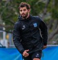 A bearded man in a black puffer jacket with what appears to be a teal team logo stands on a sports field, looking toward the camera with a serious expression. The caption "pula, get off the ground" suggests he is a coach or staff member giving directions to a player named Pula, urging them to rise from the ground—possibly after a tackle or fall during a match or training session.
