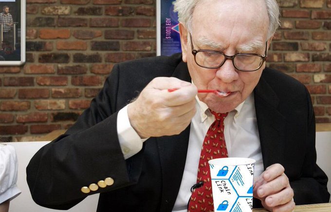 The image features a man wearing glasses and a suit eating ice cream with a spoon while sitting at a table. The man appears to be dressed for work or a formal event. In the background, there are two posters hanging on the wall behind him. The main focus of the image is the man's action of eating ice cream using a spoon, which could be related to the post about blockchain and cryptocurrency that emphasizes the importance of understanding complex topics in depth.