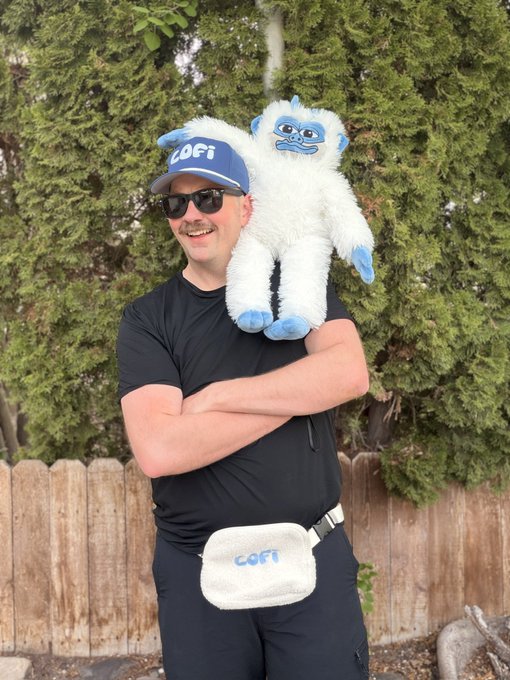 The image features a man wearing sunglasses, holding a stuffed animal, possibly a snowman or a white gorilla, over his shoulder. The man appears to be posing for a photo with the stuffed animal. The background of the image shows a fence and trees, creating an outdoor setting. There is also text in the image that reads "Main highlights on why @lofitheyeti is primed for success $LOFI holder count is steady overall, 25,000+ $LOFI social activity is actually ramping up $LOFI is doing more volume than other culture coins on @SuiNetwork and even tech projects JOIN THE FLURRY". This suggests that the man might be promoting a product or service related to the stuffed animal he's holding.