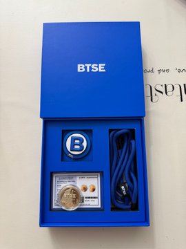 A blue BTSE branded gift box containing a BTSE branded medallion/coin, a USB security key, and a blue USB cable, displayed on a white surface.