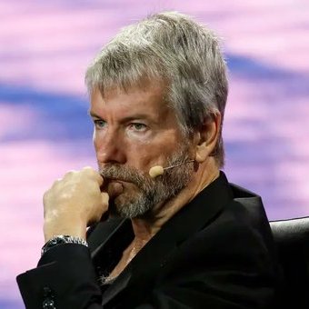A man with gray hair and a beard, wearing a black suit and a headset microphone, listens intently with his hand near his chin during what appears to be a conference or panel discussion. The image accompanies a post discussing massive unrealized cryptocurrency losses held by Strategy ($14 billion in Bitcoin) and Bitmine ($10.5 billion in Ethereum), likely depicting one of the executives mentioned.
