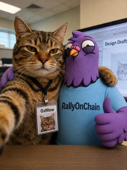 The image features a cat wearing a name tag that says "OxMaw" and a stuffed animal bird with a purple shirt, both of which are sitting at a desk next to each other. The cat appears to be taking a selfie using its phone while the bird is giving it a thumbs up. The background shows an office setting with a computer monitor on the wall behind them.