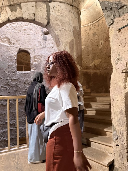 A woman with curly red hair stands unaware as she appears to pose for a photo in a stone archway.