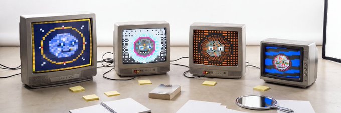 Four vintage CRT televisions are lined up on a desk, each displaying a different pixel-art circular design in blue, pink, orange, and red color schemes, with a magnifying glass and sticky notes scattered in front.
