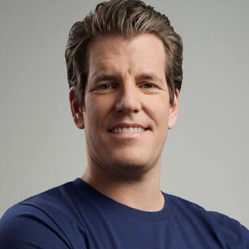 The image features a man with short brown hair wearing a blue shirt, smiling at the camera. The background of the photo is white, which contrasts with the man's dark hair. There are no other objects or texts present in the image. The caption above the photo reads """Wait till the world realizes that Bitcoin is Gold 2.0."- Tyler Winklevoss". This text seems to be related to the content of the image and could possibly be a reference to the cryptocurrency market, Bitcoin, which has been gaining popularity recently.