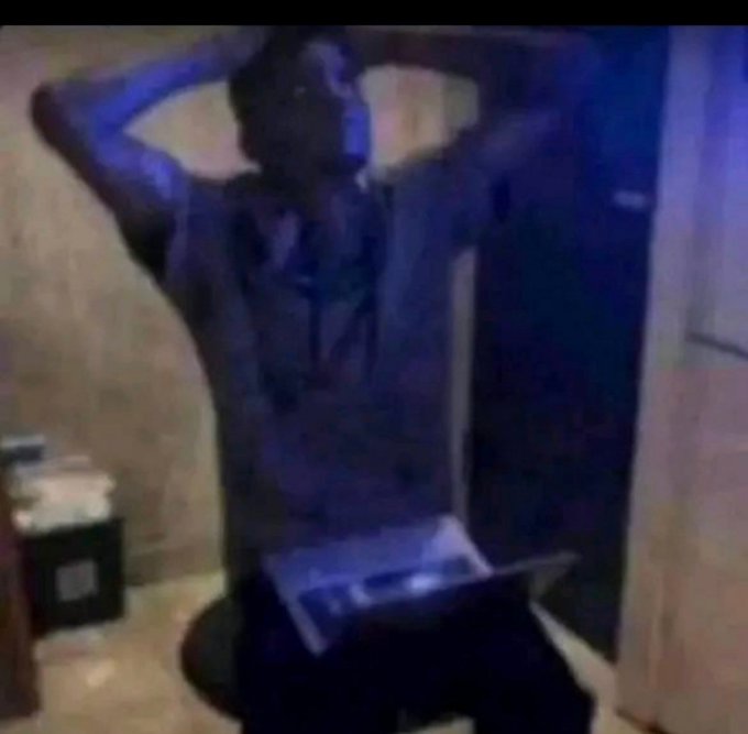 A blurry, low-quality video still shows a person sitting in a dimly lit room with their hands on their head, wearing headphones and facing a laptop or screen.