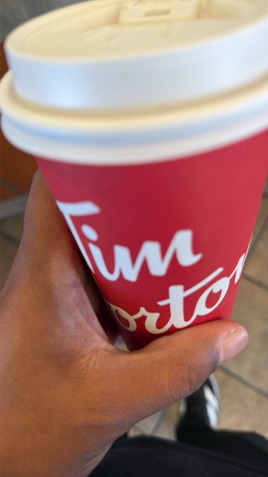 A hand holds a red Tim Hortons coffee cup with a white lid, with partial text reading 'Tim' and 'orto' visible.