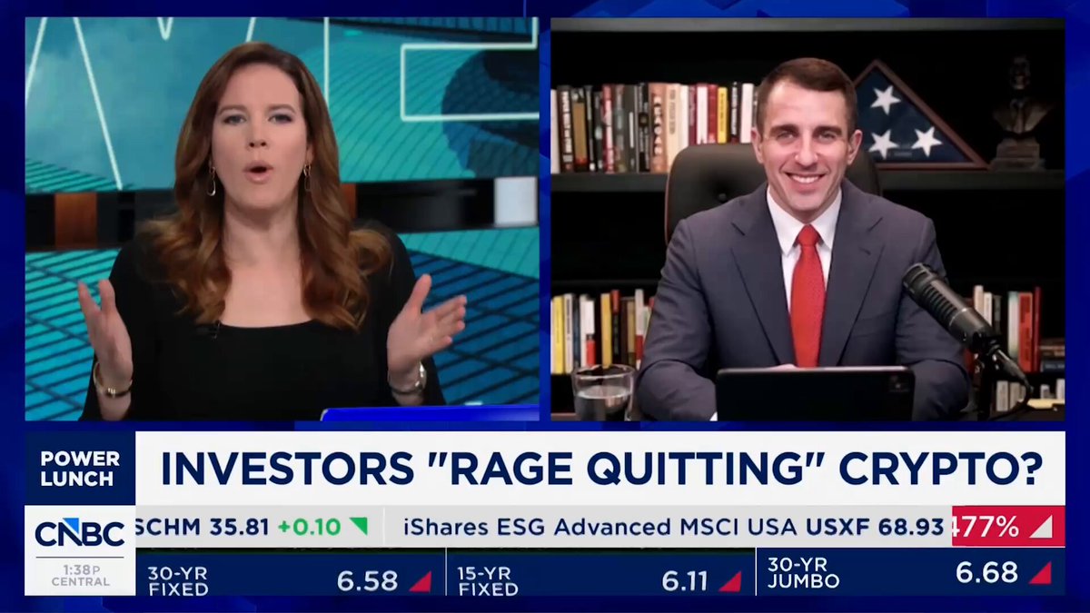 The image shows a news segment featuring two people sitting at a desk with a laptop computer. One person appears to be a woman wearing a black top, while the other person is a man dressed in a suit and tie. They are both talking about Bitcoin and its potential uses for protecting assets against government spending or economic instability. The background of the image features a blue sky and clouds, suggesting that they might be discussing this topic during an outdoor event or gathering.