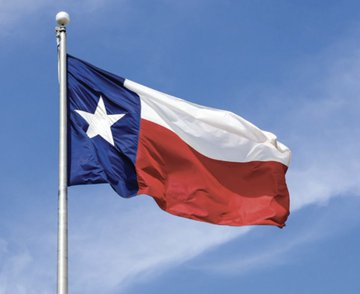 The Texas state flag waves against a blue sky, symbolizing the state's bold embrace of Bitcoin as described in the post about Governor Greg Abbott positioning Texas as the "Mecca of Bitcoin," housing a significant share of global mining operations and becoming the first state to hold BTC in a strategic reserve.