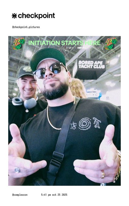 The image shows two men posing for a photo, with one man wearing sunglasses and holding his hands out as if he's about to do something. The other man has a camera around his neck, suggesting they are taking a picture together. The background of the image is white, which contrasts with the black t-shirt worn by the first man. There is also text in the image that reads "checkpoint", indicating it might be an article or post related to the men's activities at the yacht club.
