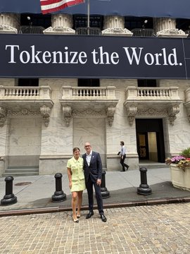 A man in a suit and a woman in a yellow dress stand in front of the New York Stock Exchange beneath a large banner reading "Tokenize the World.," celebrating Securitize's CEO @carlosdomingo ringing the closing bell for $SECZ at the NYSE.