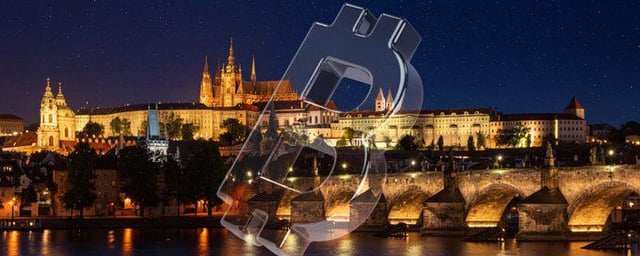 A nighttime panoramic photograph of Prague Castle and the Charles Bridge over the Vltava River, overlaid with a faint watermark of a 'B' logo.