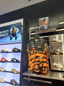 The image shows a PUMA store display featuring an orange and black racing-style jersey with OKX sponsorship logos, alongside shelves of sneakers and a digital screen displaying "RAGE MEETS INSTINCT" with an athlete. The post highlights the OKX brand partnership with PUMA, showcasing their collaborative merchandise and expressing appreciation for the sponsorship of major global sporting events.