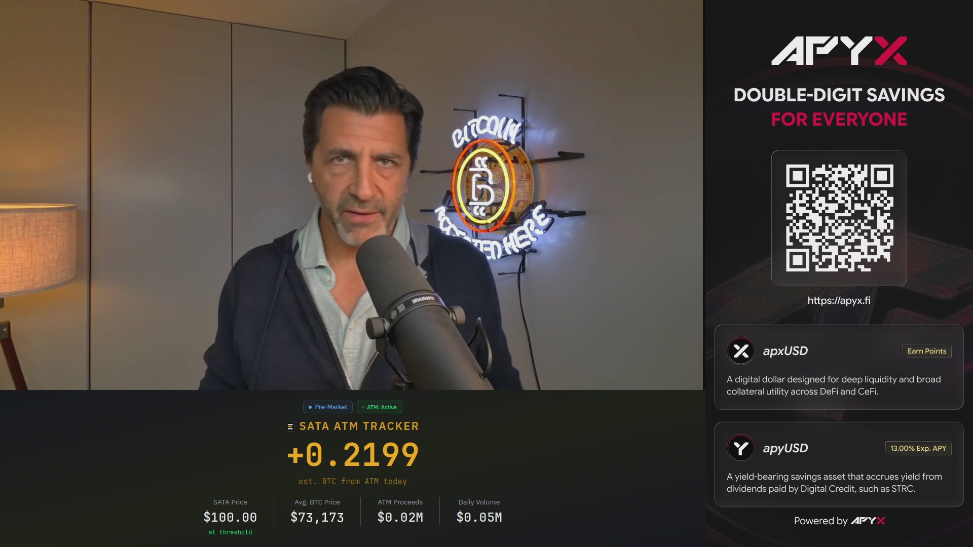 The image shows a man standing next to a microphone, with a computer screen behind him displaying information about Bitcoin accumulation. The text on the screen reads "Just In: Strive's $SATA #Bitcoin accumulation for today has just started in pre-market. Powered by @Apyx_fi | Double-digit yield for everyone. TRACK IT LIVE:". This suggests that the man is likely a Bitcoin enthusiast or an early adopter of this digital currency, and he might be discussing the current state of Bitcoin accumulation with others through live streaming or social media platforms.