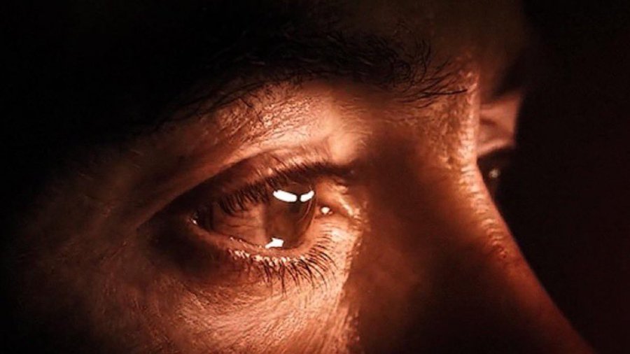 An extreme close-up of a person's brown eye in dramatic, warm lighting, highlighting the iris details and surrounding skin texture.