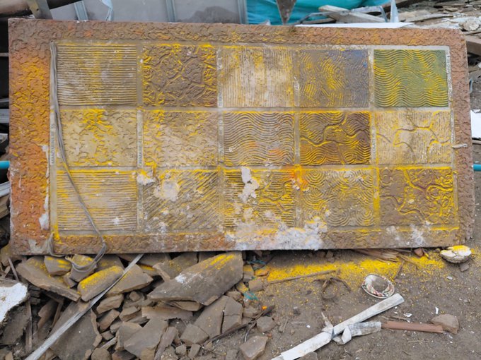 A heavily weathered, rust-stained decorative concrete block with yellow paint residue lies among construction rubble and broken tile pieces.