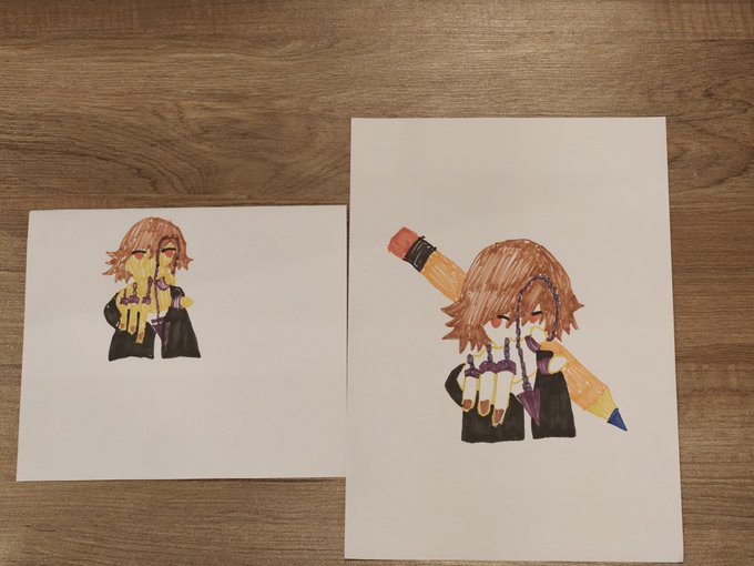 Two anime-style marker drawings on white paper of a character with brown hair covering their face, displayed on a wooden surface.