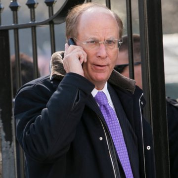 A man in a dark coat, glasses, and purple tie is talking on a mobile phone outdoors.