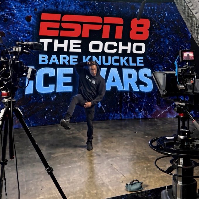 A man poses dramatically in an ESPN 8 "The Ocho" studio set with a "Bare Knuckle Dice Wars" backdrop, surrounded by professional camera equipment, promoting the upcoming Pulsechain marketing appearance scheduled for 10:30 pm EST.
