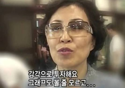 A woman wearing glasses speaks while Korean subtitles appear at the bottom reading "갑작으로 투자해요 그래도 표도 볼 줄 모르고..." (roughly: "I invest all of a sudden, but I can't read the chart...").

The image, appearing to be a screenshot from an older Korean stock market TV segment, visually contrasts with the post's commentary about market trends — the woman's bewildered expression and dialogue about not knowing how to read charts echo the poster's skepticism about blindly trusting others' bullish claims, as both highlight uncertainty and confusion surrounding market direction.