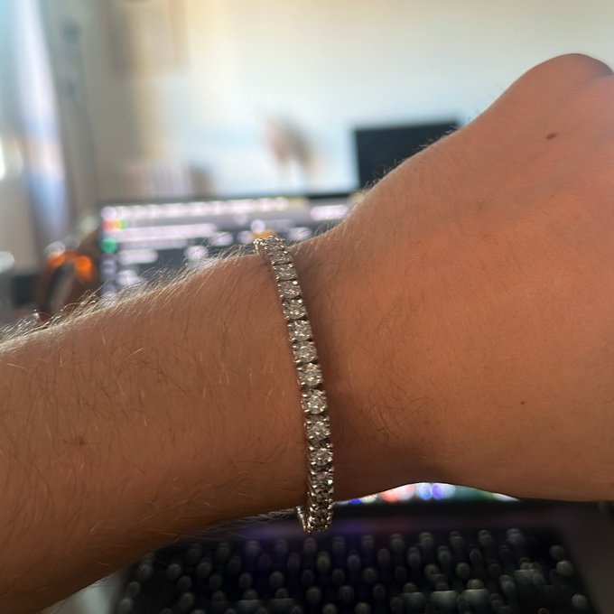 A close-up shot of a person's wrist wearing a sparkling diamond tennis bracelet, with a blurred computer setup visible in the background. The image showcases a luxurious accessory, fitting the post's theme of celebration and generosity within the Web3 community.