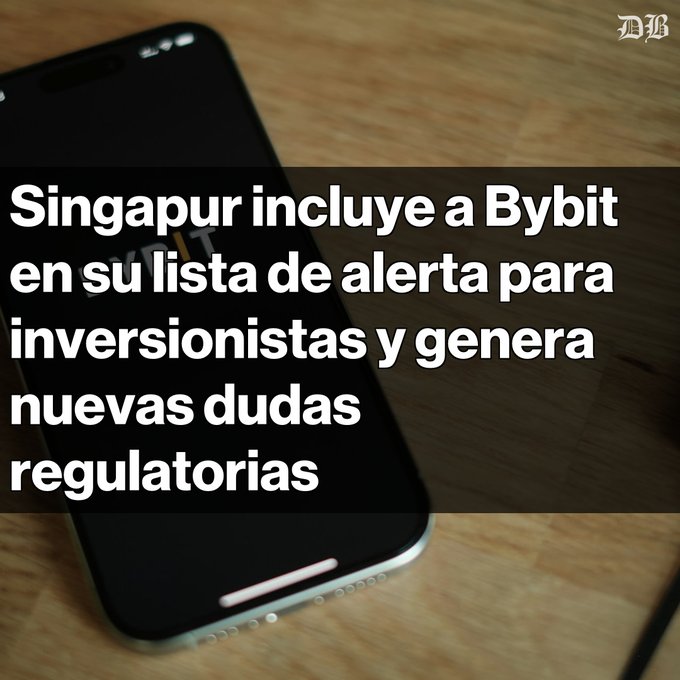 The image shows a black smartphone laying flat on a wooden surface, with text written above and below it that reads "Singapur incluye a Bybit en su lista de alerta para inversionistas y generalistas Advertencia en Singapur". The phone is positioned at the bottom of the image.