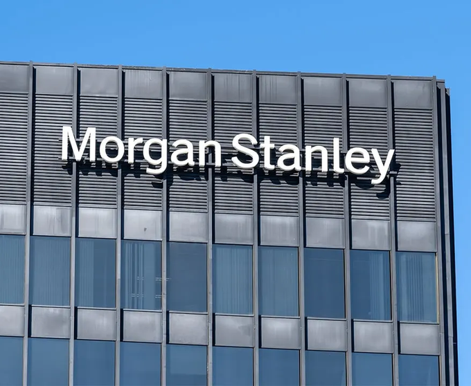 The Morgan Stanley logo is displayed prominently on the upper portion of a modern glass office building against a clear blue sky, with the company name in white lettering. This image relates to the news of Morgan Stanley revealing $1.6 trillion in XRP exposure, highlighting the financial giant's involvement with the cryptocurrency.
