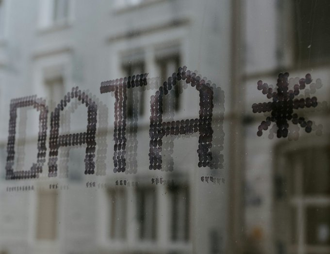 The word 'DATA' with an asterisk appears as dotted text on a glass window, with a building visible in the blurred reflection.