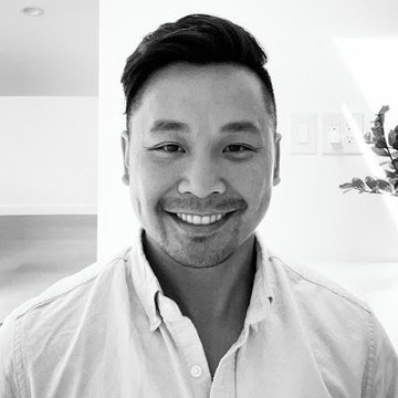 A black-and-white headshot of a smiling man with short dark hair wearing a light-colored button-up shirt.