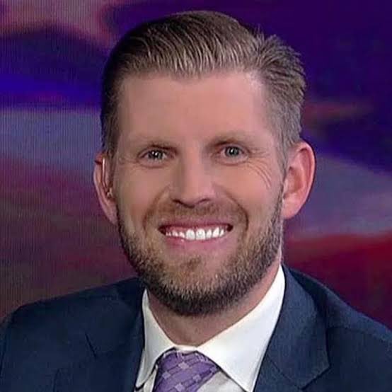 Eric Trump is shown smiling in a suit and purple tie during what appears to be a televised interview, while the caption humorously warns about the WLFI coin's token unlock event, implying that despite a low-point unlocks, the "umbrella" (protection) won't open—advising viewers to stay away from the project.