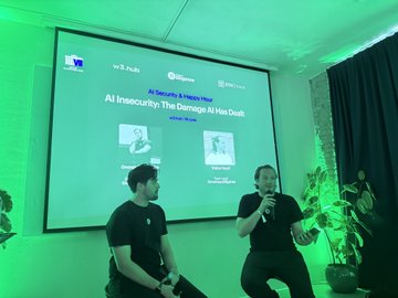 Two men sitting on stools on a stage during a panel discussion titled 'AI Financing? The Damage AI Has Done' in a green-lit room.