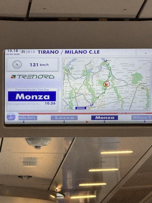 A digital display inside a Trenord train shows the route from Tirano to Milano C.LE, traveling at 131 km/h, with the next stop being Monza at 10:26 on 06/09/2026.
