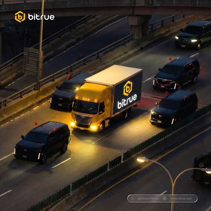 The image shows a busy highway with multiple cars driving down it at night. There are several trucks on the road as well, including one that has "bitrue" written on its side. The text in the image suggests that there might be an advertisement or promotion related to Bitcoin or cryptocurrency.