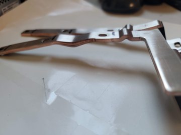 A metallic, gun-shaped object rests on a light-colored surface next to some clear plastic packaging.