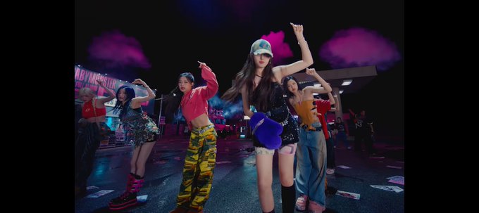 A group of women perform a choreographed dance in what appears to be a music video setting, with dramatic stage lighting and smoke in the background.