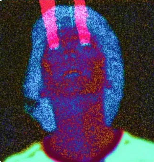 A heavily stylized, glitchy/psychedelic image with a blue, pink, and orange color palette showing what appears to be a distorted figure or face against a dark textured background.
