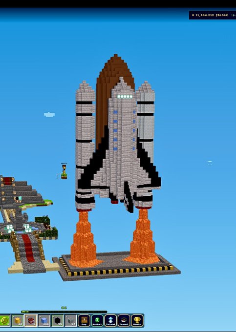 A screenshot from the game Minecraft showing a large pixel art statue of a space shuttle with the word 'NASA' on it, built with orange rocket boosters at the base.