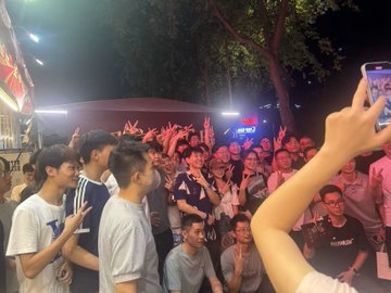A dense nighttime crowd gathers at an outdoor event, with many attendees raising their hands and holding up smartphones to record or take photos, while someone in the foreground films the lively scene on a phone. The image reflects the post's playful reference to "EnHeng456," capturing the kind of packed, enthusiastic gathering where people might jokingly note the absence of 20-year-old Sun Yuchen but the presence of a lively crowd reminiscent of the trending topic.