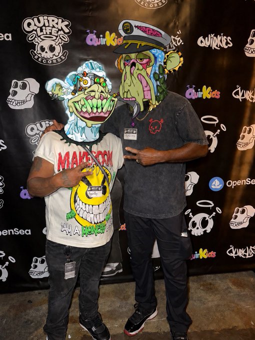 Two people pose in front of a "Quirk Life Records" and "QuirKids" backdrop, but their faces have been digitally replaced with grotesque clown/monster cartoon masks.