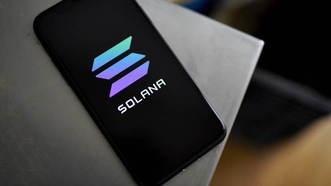 A smartphone displays the colorful Solana logo and name on a black background, resting on a light surface, visually representing the article's focus on the Solana blockchain network and its efforts to build public trust.