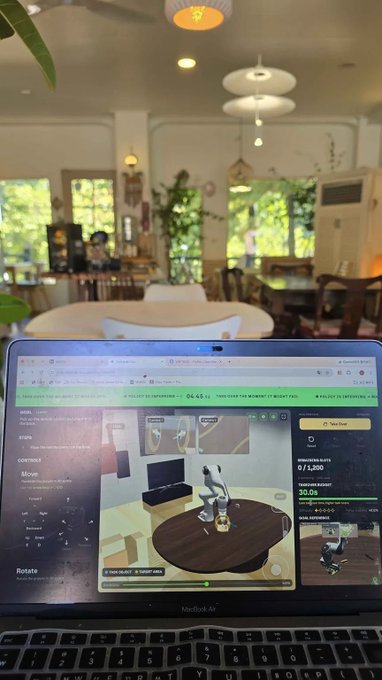 A MacBook Air laptop sits open on a table in a sunlit cafe, displaying a 3D design software interface with rendering settings on screen.
